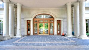La entrada de un edificio con un gran arco adintelado flanqueado por columnas, que conduce a un área de recepción con pavimento de baldosas.