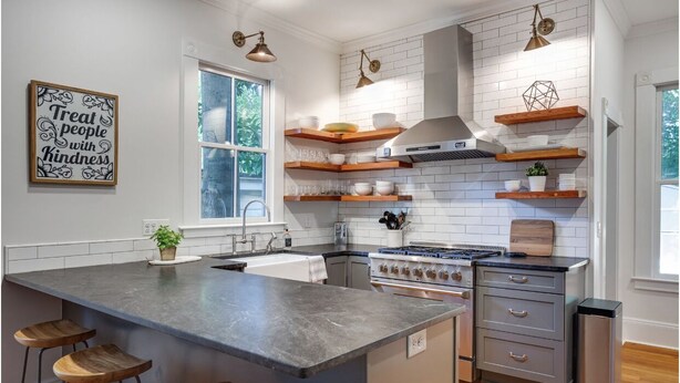 Una cocina moderna con una isla grande, taburetes de bar de madera, baldosas blancas tipo metro y estantes empotrados.