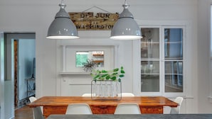 Un comedor con una mesa de madera, sillas blancas y dos lámparas colgantes. Un cartel sobre la mesa dice "DE JURE TO WASHINGTON".