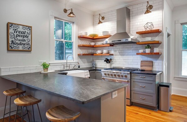 A modern kitchen with a large island, wooden bar stools, white subway tiles, and built-in shelves. - Historic Oakwood Hideaway (Raleigh)