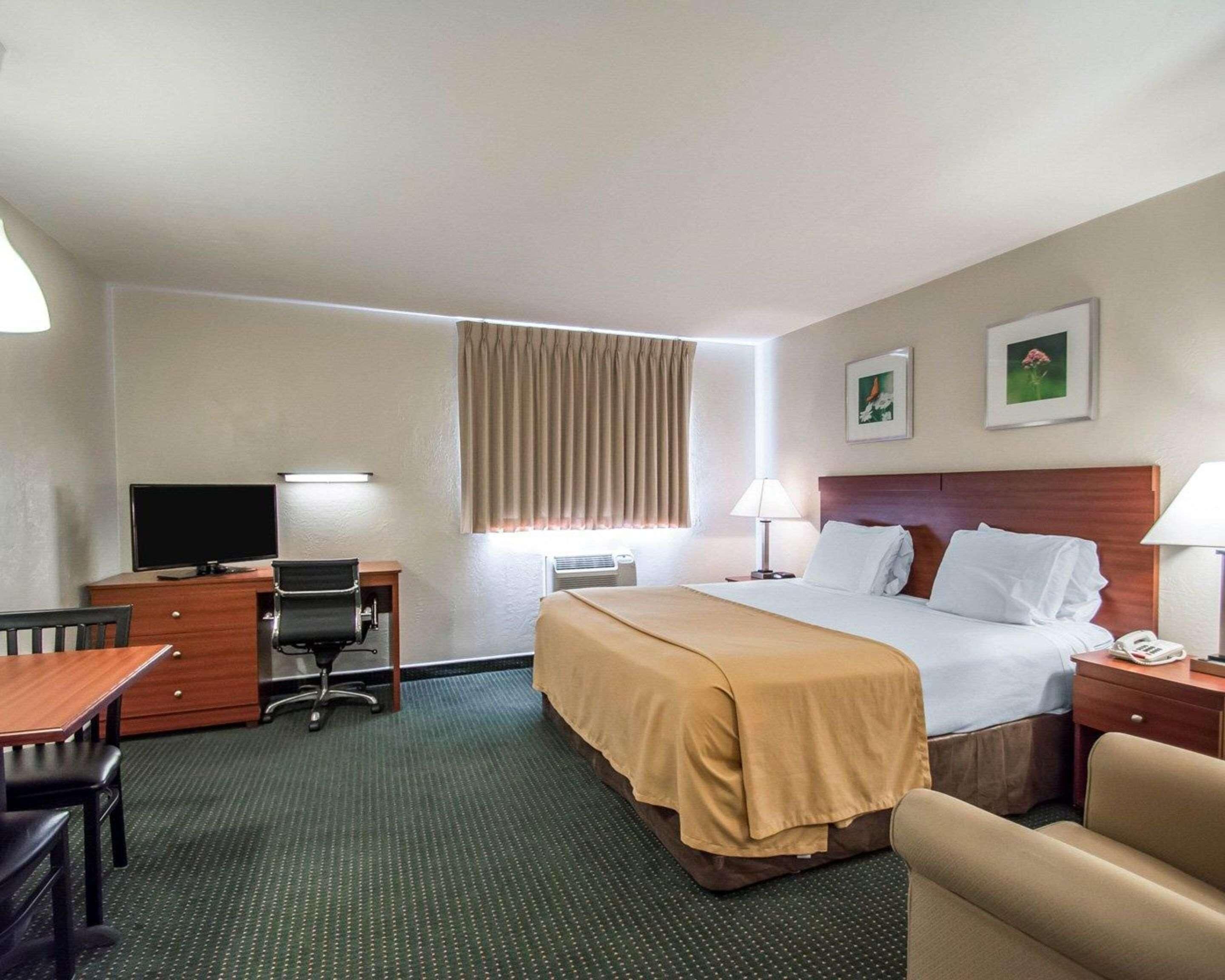 A hotel room with a bed, desk, chair, TV, and two framed pictures on the wall.