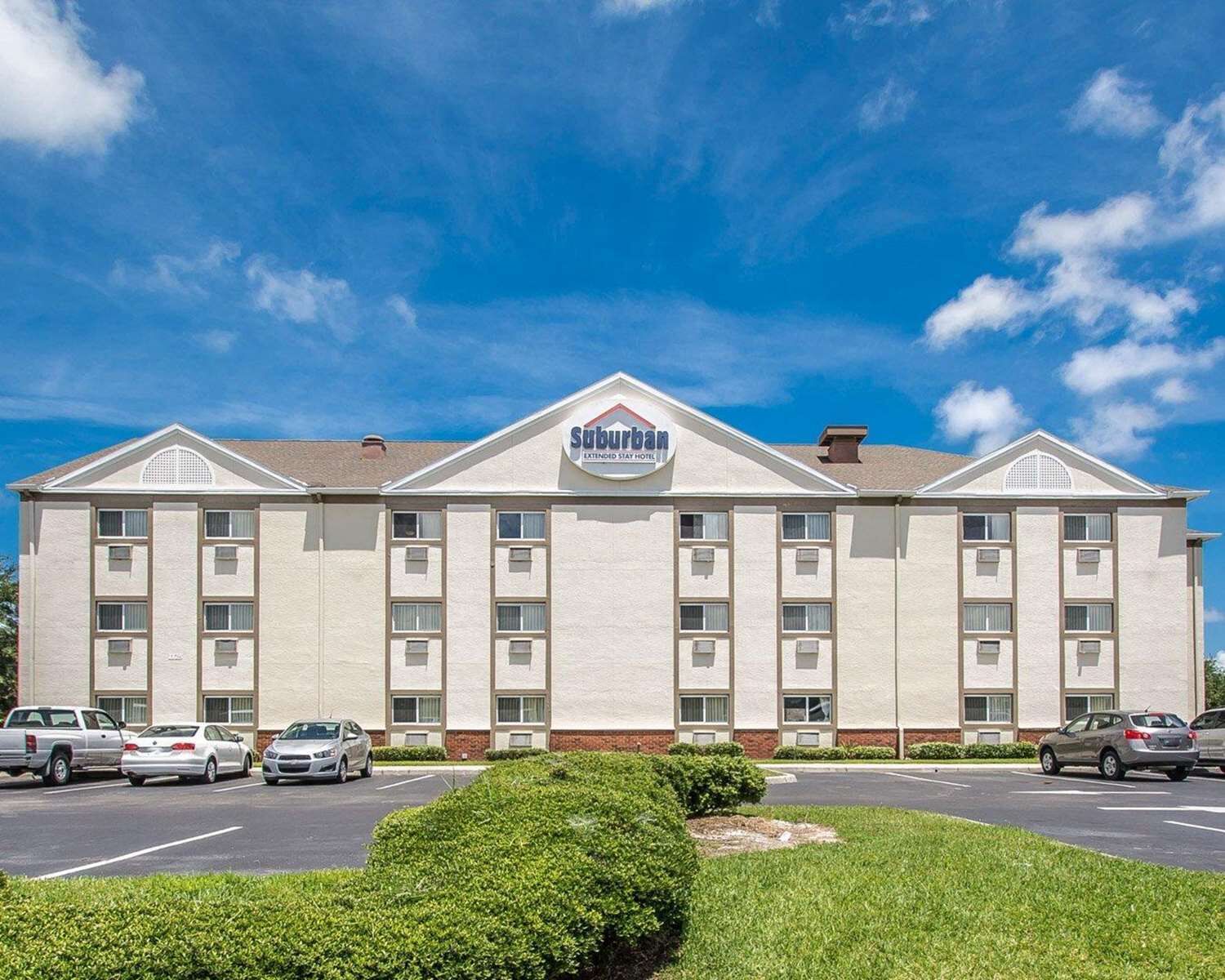 Un hotel para estancias prolongadas en las afueras, con una fachada simétrica, múltiples ventanas y un estacionamiento con varios automóviles.