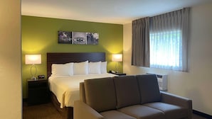 Ein Hotelzimmer mit Bett, zwei Nachttischlampen, einem Sofa, einem Fenster mit Vorhängen und einem Wandbild.