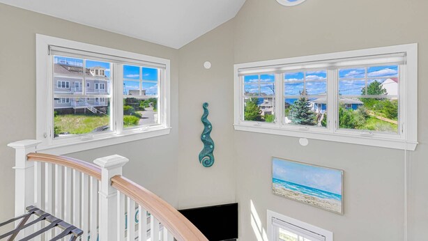 Una habitación con dos ventanas amplias que dan vistas a un barrio residencial, una lámpara de techo y un adorno en la pared.