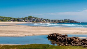 Una playa con casas al fondo y un promontorio rocoso al frente.