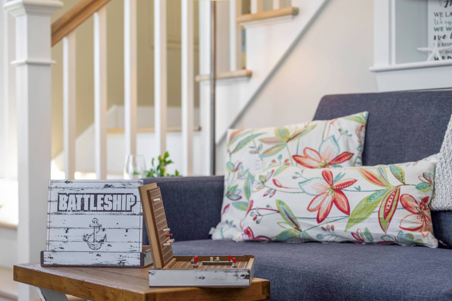 Eine Holzkiste mit dem Schriftzug 'RAILSHIP' und einem Anker, ein kleines Holzmodell auf einem Tisch sowie eine Couch mit Blumenkissen.