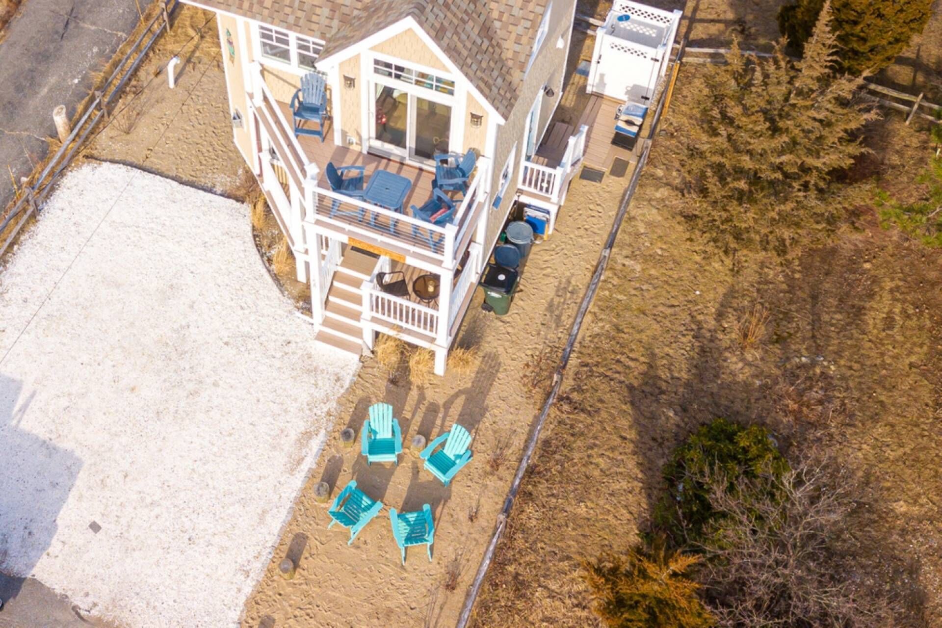 Une maison à deux étages dotée d’un balcon, d’une terrasse et d’un espace sablonneux avec des chaises.