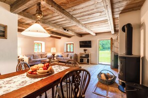 A cozy living room with a wooden ceiling, a dining table with a fruit basket, a sofa, and a fireplace. - Vacation home Nöstlbach - Country house with garden (Pittenhart)