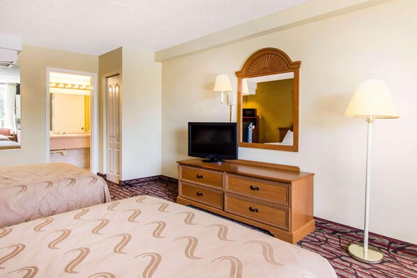 A hotel room with two beds, a television on a wooden dresser, a mirror, and a floor lamp. - Rodeway Inn Central Clearwater Beach (Clearwater)