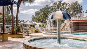 A pool area with a central fountain, surrounded by palm trees and a covered seating area. - Rodeway Inn Central Clearwater Beach (Clearwater)