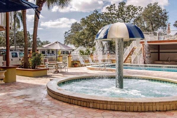 A pool area with a central fountain, surrounded by palm trees and a covered seating area.