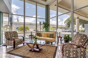 A spacious lobby with large windows, a sofa, patterned chairs, a coffee table, and a potted plant.