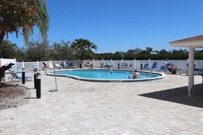 A swimming pool with a tiled deck, surrounded by lounge chairs and a white fence.
