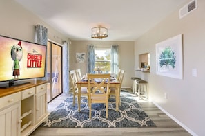 A dining area with a table set for four, a television displaying 'Chicken Little', and a chandelier.