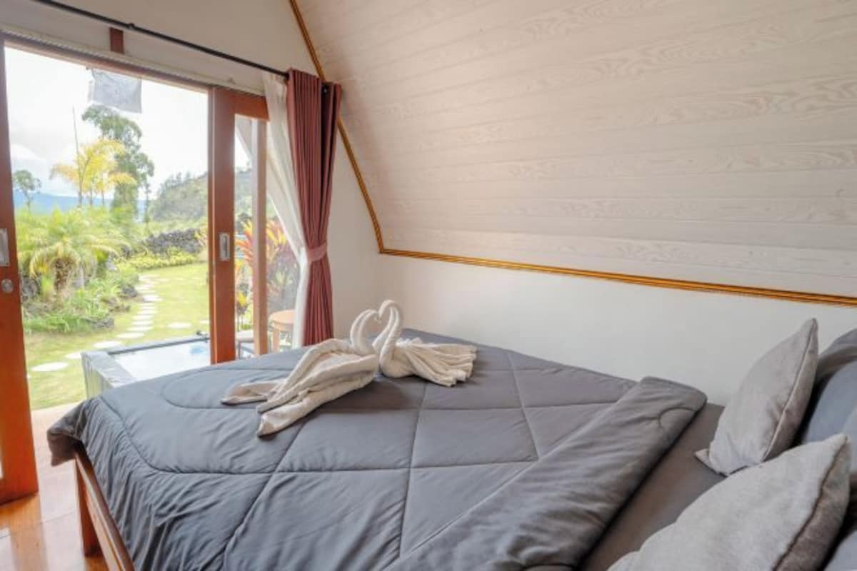 Un dormitorio con una cama grande, vista a un jardín y una piscina, y una puerta corrediza de vidrio.