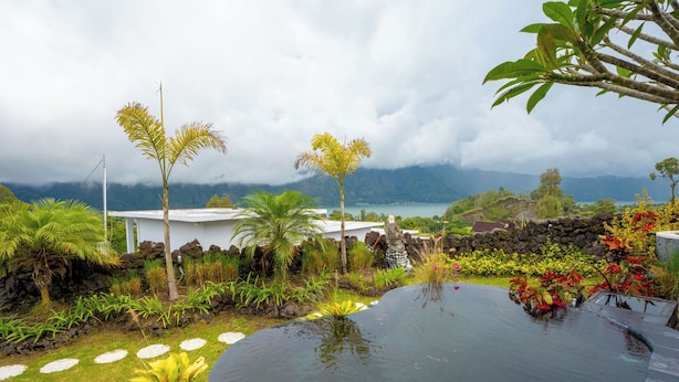 A tropical garden with a swimming pool, lush greenery, and a view of mountains and a lake. - Break Villa Kintamani (Kintamani)