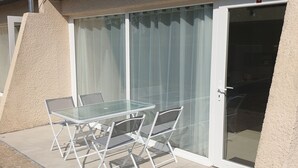 Patio esterno con tavolo e sedie in vetro, una porta scorrevole in vetro e un muro dalla superficie strutturata.