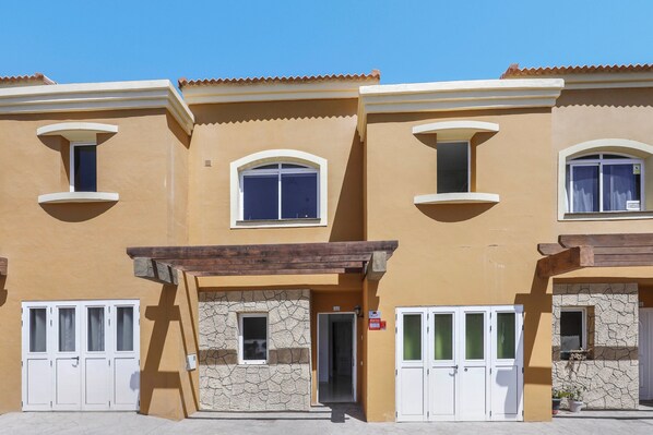 A row of three-story buildings with balconies, a stone facade, and a tiled roof.