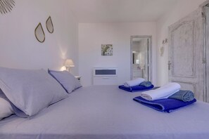 A bedroom with a bed, pillows, a TV, a bedside table, and a door.