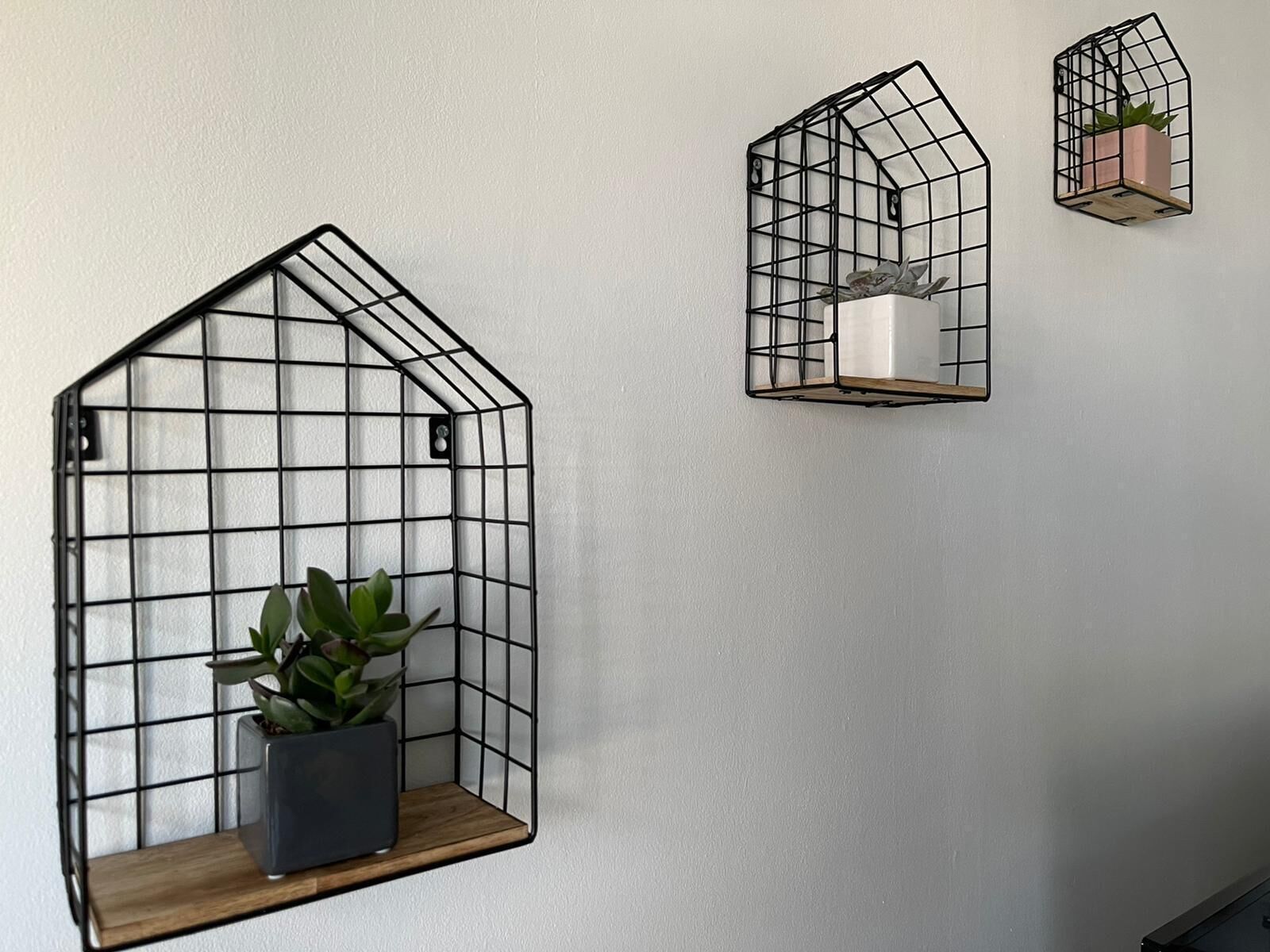 Three black metal wall-mounted shelves with a grid design, each holding a potted plant.
