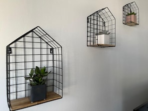 Three black metal wall-mounted shelves with a grid design, each holding a potted plant.