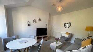 Een moderne woonkamer met een ronde eettafel, grijze banken, een flatscreen televisie en decoratieve wandkunst.