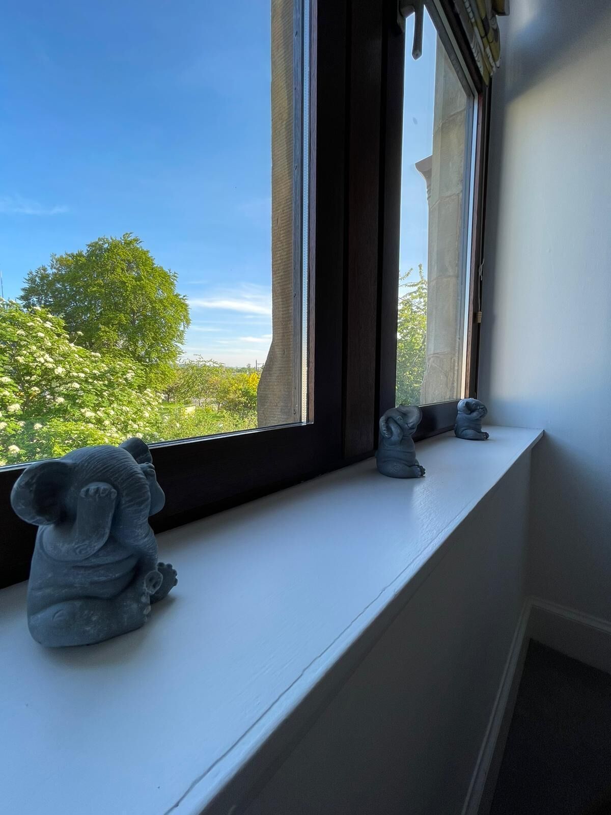 Un rebord de fenêtre orné de trois statuettes d’éléphants, avec vue sur des arbres et un bâtiment à l’extérieur.