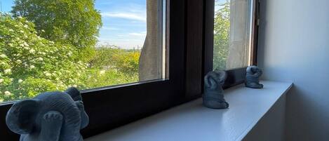 Un rebord de fenêtre orné de trois statuettes d’éléphants, avec vue sur des arbres et un bâtiment à l’extérieur.