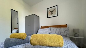 Een hotelkamer met een bed, een kledingkast, een spiegel, een ingelijst schilderij en een nachtkastje met een lamp.