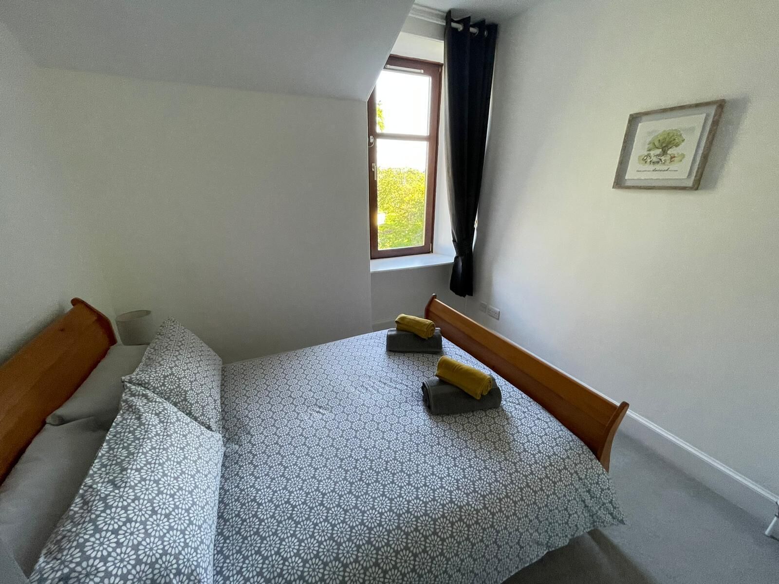 A bedroom with a bed, a window with curtains, and a framed picture on the wall.