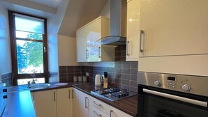 Een moderne keuken met witte kasten, een Bosch oven, een gasfornuis en een raam met uitzicht op bomen.