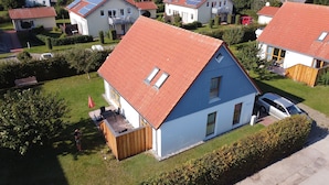 Ein Wohnhaus mit rotem Satteldach, einem kleinen Anbau aus Holz und einer gepflasterten Terrasse mit Gartenmöbeln.
