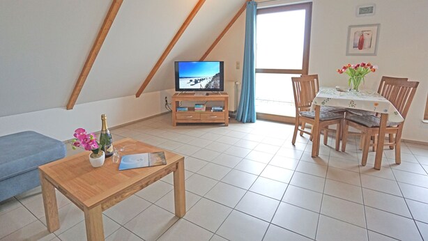 Ein gemütliches Wohnzimmer mit Holztisch, Fernseher und Essbereich mit Stühlen und Tisch.