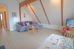 Una sala de estar acogedora con un sofá azul, una mesa de centro de madera y un televisor sobre un mueble de madera.