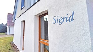 A building with a white exterior and a window with a wooden frame. The word "Sigrid" is painted on the wall.