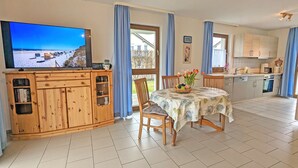 En hyggelig stue med TV, et træskab, et spisebord med stole og et køkkenområde.