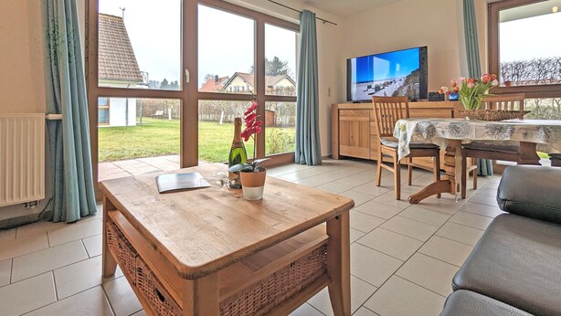 A spacious living room with a wooden coffee table, a television, and a dining area with a table set for two.