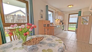 A kitchen with a dining area, a window with curtains, and a vase of tulips on the table.