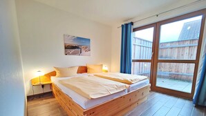 A wooden bed with two pillows, a nightstand with a lamp, a window with curtains, and a picture on the wall.