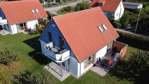 A two-story house with a red roof, a balcony with outdoor furniture, and a small garden area.