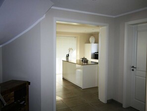 A narrow hallway leading to a kitchen with a central island, white cabinetry, and a tiled floor.