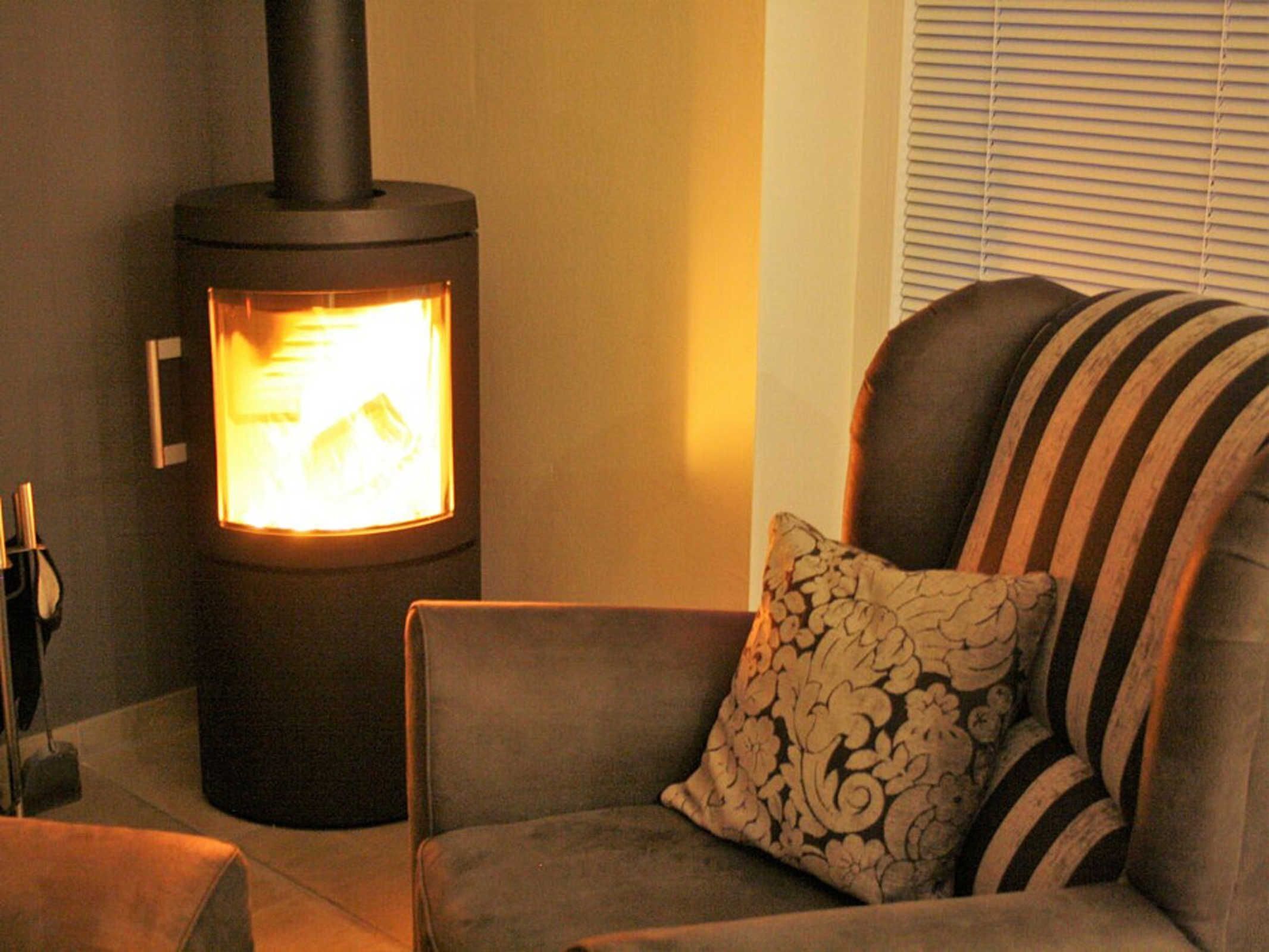 A room with a wood-burning stove, a sofa, and a patterned pillow.