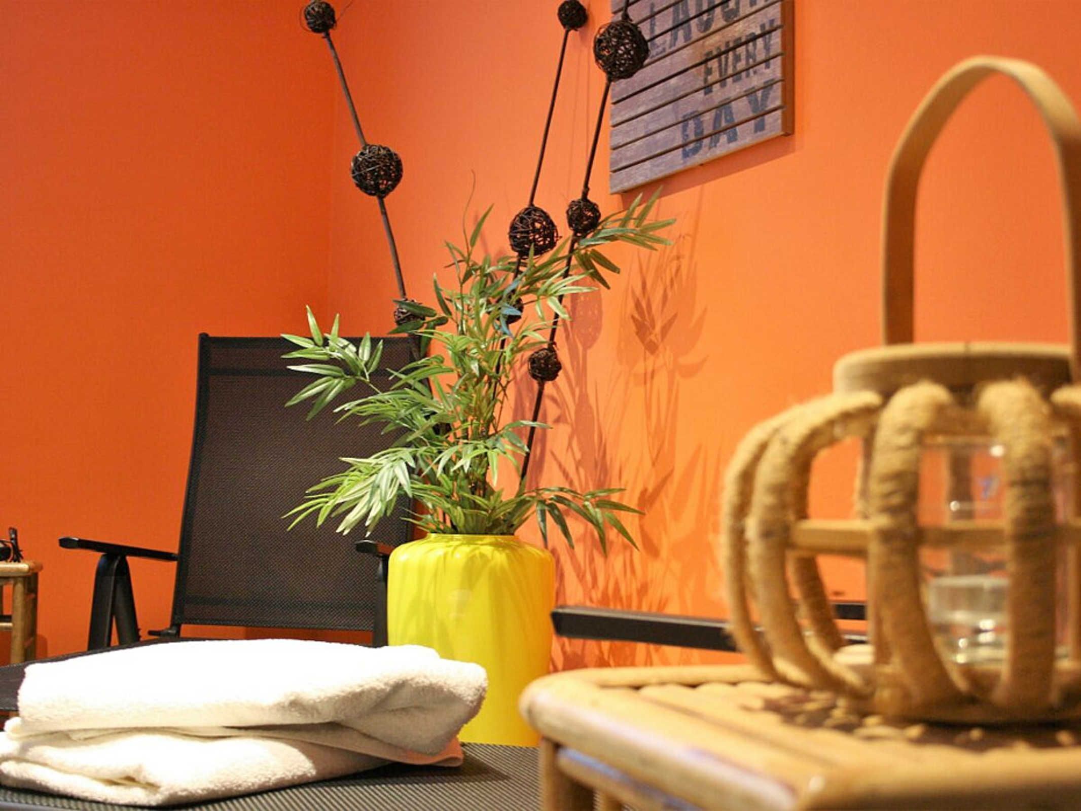 Una habitación con una silla, un jarrón amarillo con una planta y una toalla sobre una mesa.