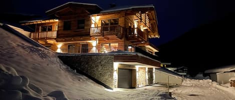 Un edificio de madera de varios pisos con balcones, una entrada de piedra y una ladera cubierta de nieve.