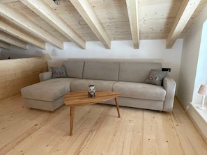 A room with a wooden ceiling, a grey sectional sofa, a wooden coffee table, and a lamp.
