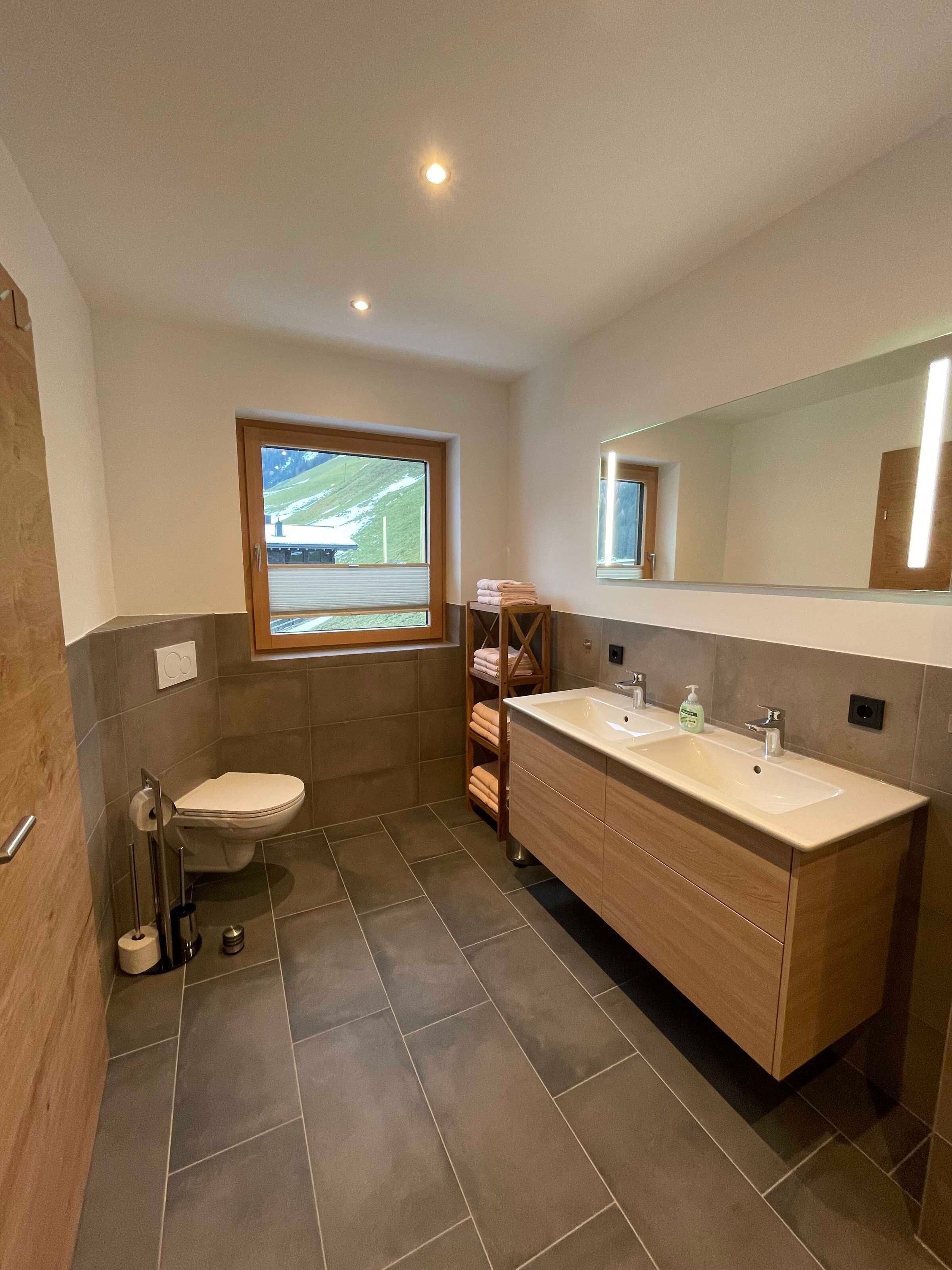 Ein modernes Badezimmer mit Toilette, Waschbecken, Spiegel und Fenster.