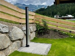 Un muro de piedra con un poste metálico, una valla de madera y una zona verde con vistas a montañas.