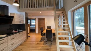 A modern kitchen with wooden cabinets, a dining area with a table and chairs, and a staircase leading to an upper level. - Apartment Edelweiss - TUX MOUNTAIN apart (Juns)