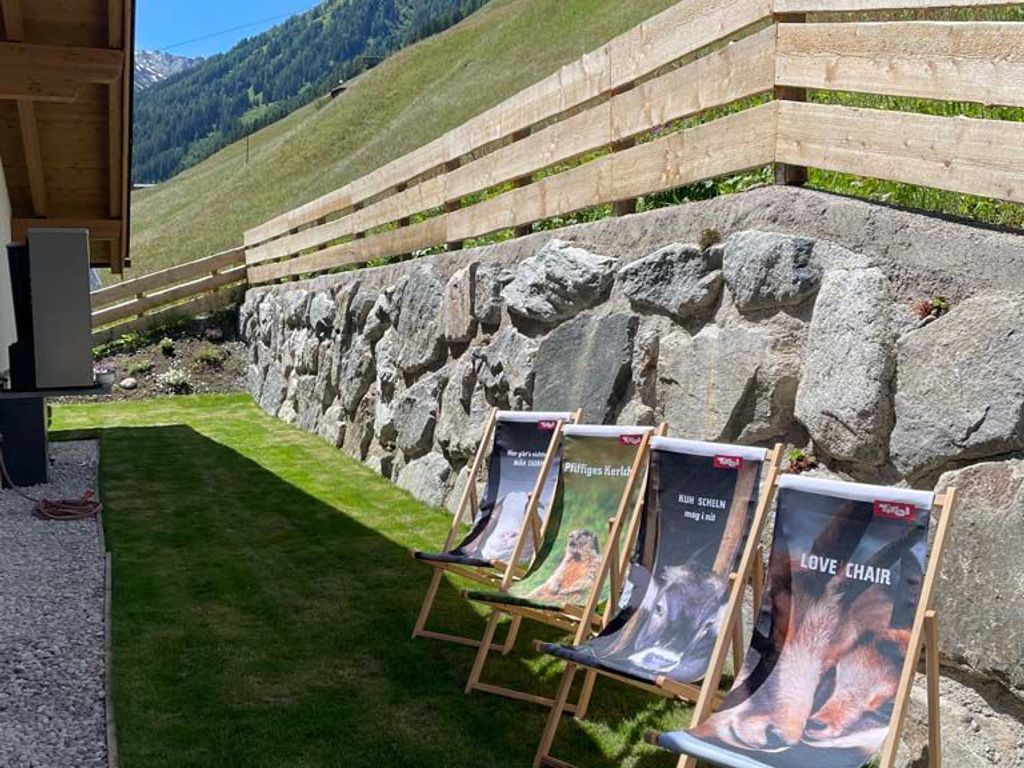 Espace extérieur aménagé avec des affiches, un mur de pierre et une zone herbeuse, le tout avec une vue sur les montagnes en arrière-plan.