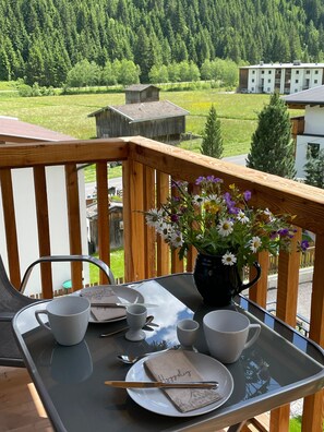Ein Balkon mit Tisch für zwei Personen, einem Blumenstrauß und Blick auf eine bewaldete Gegend.